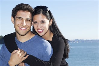Smiling mixed race couple hugging by water