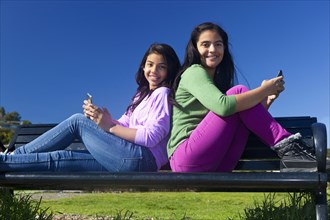 Hispanic teenage girls sitting on park bench