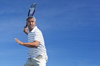 Mixed race man playing tennis outdoors
