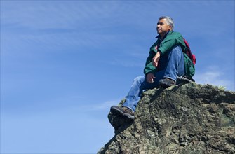 Mixed race man sitting on rocky hilltop