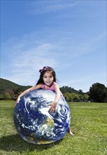 Mixed race girl playing with globe in park