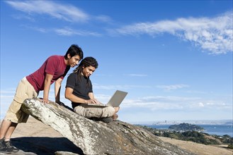 Men using laptop on rocky hilltop