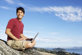 Climber using laptop on rocky hilltop