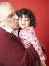 Senior Hispanic man kissing granddaughter