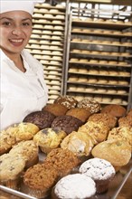 Hispanic baker carrying tray of muffins in bakery