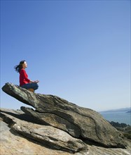 Asian woman meditating on rock formation