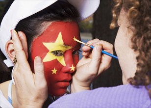 Woman painting Chinese flag on Chinese girl's face