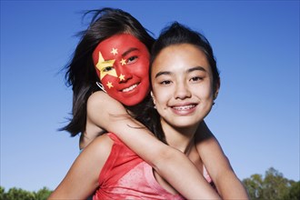 Chinese girl with Chinese flag painted on face hugging friend