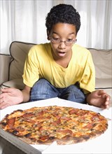 Mixed race boy admiring pizza in living room