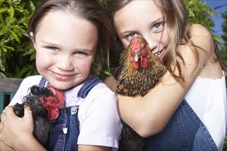 Mixed race girls holding chickens on farm
