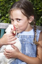 Mixed race girl kissing chicken on farm