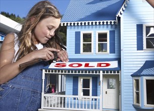 Mixed race girl putting 'sold' sign on doll house