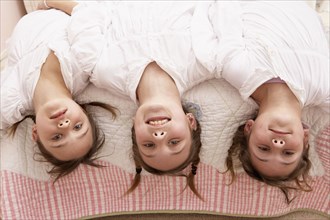 Mixed race girls hanging upside down from bed
