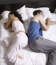 Couple sleeping back-to-back on bed