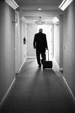 Caucasian businessman pulling luggage in hotel hallway