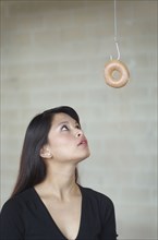 Asian woman looking at doughnut on hook