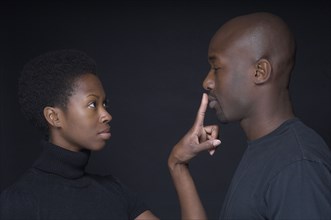 African woman putting finger on boyfriend's lips