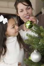 Hispanic mother and daughter decorating Christmas tree