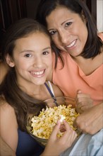 Hispanic mother and daughter eating popcorn