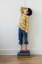 Asian boy standing on books in front of height markers