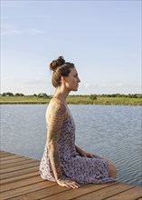 Caucasian woman sitting on wooden dock over lake