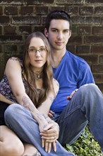 Caucasian couple sitting on ground leaning on wall