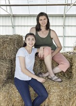 Portrait of smiling Caucasian mother and daughter sitting on hay bales
