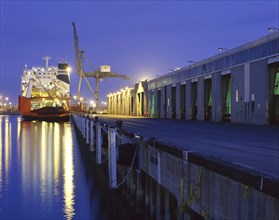 Cargo ship under crane in harbor at night