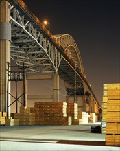 Piles of lumber under bridge at night