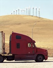 Red semi-truck parked near wind farm