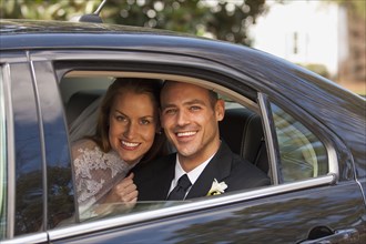 Caucasian bride and groom in back seat of car