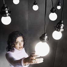 Young woman reaching up to grasp a light bulb