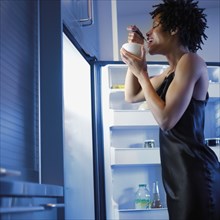 African woman eating next to open refrigerator