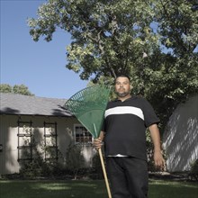 Hispanic man standing in yard with rake