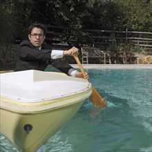 Mixed race businessman rowing boat in swimming pool