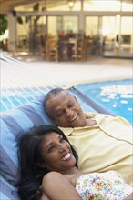 Multi-ethnic couple laying in hammock at poolside