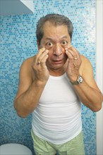 Hispanic man looking at his eyes in bathroom