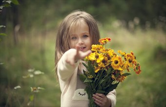 Smiling Caucasian girl pointing finger and holding flowers