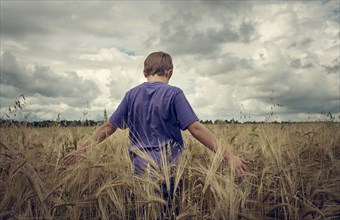Caucasian boy walking in field of wheat