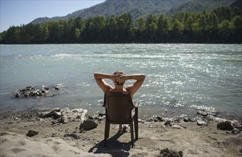 Caucasian man sitting in chair sunbathing near river
