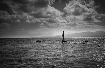 Silhouette of Caucasian boy standing on rock in ocean