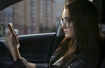 Caucasian woman sitting in car texting on cell phone