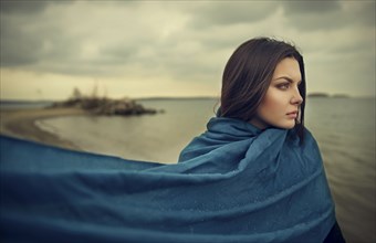Wind blowing blue blanket of Caucasian woman at beach