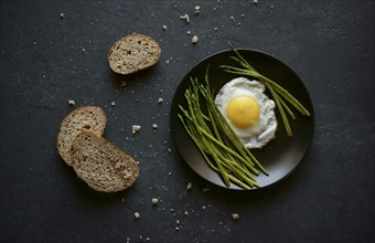 Bread and crumbs near plate with fried egg and asparagus
