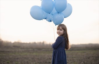 Caucasian girl holding blue helium balloons