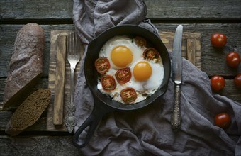 Eggs and tomatoes in frying pan on wooden table