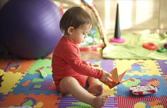 Baby boy sitting on playroom floor holding book