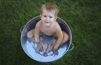 Naked Caucasian boy in metal tub in grass