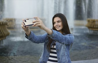 Caucasian woman posing for cell phone selfie near fountain