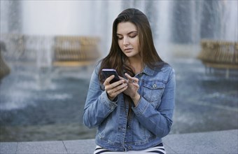 Caucasian woman texting on cell phone at fountain
